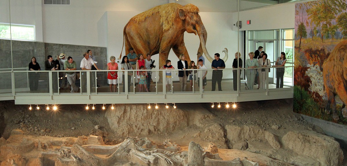 A group of people observe a mammoth exhibit from an elevated walkway in a museum in McLennan County, Texas.