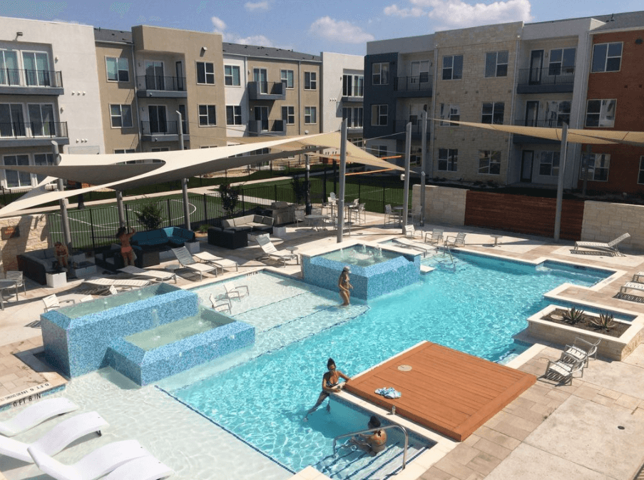 People relaxing in a modern apartment complex swimming pool area on a sunny day in McLennan County, Texas.