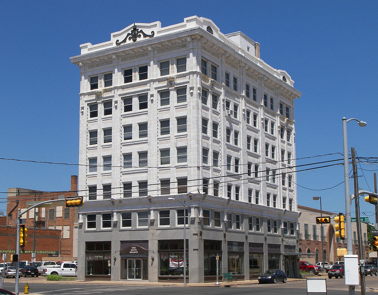 A tall, white, historic commercial building stands on a street corner under a blue sky in McLennan County, Texas.