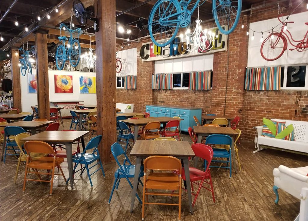 A rustic cafe interior with brick walls, wooden tables, and colorful metal folding chairs in McLennan County, Texas.