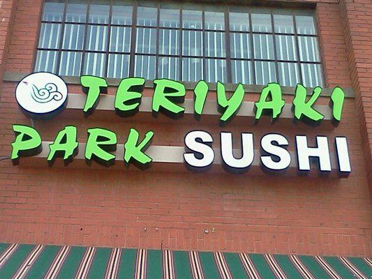 A sign for Teriyaki Park Sushi mounted on a red brick wall in McLennan County, Texas.