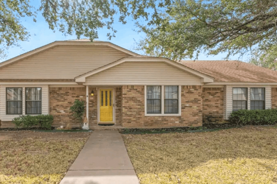 A single-story brick house with a bright yellow front door and beige siding in McLennan County, Texas.