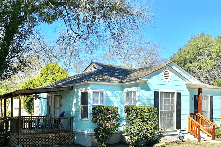 A light blue cottage-style house with a wooden porch and black shutters in McLennan County, Texas.