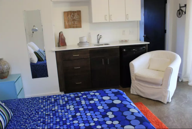 A small hotel room featuring a bed, kitchenette, and a white armchair in McLennan County, Texas.