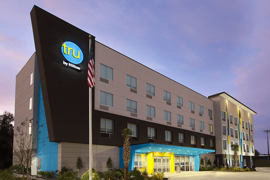 A modern Tru by Hilton hotel building exterior at dusk with an American flag in McLennan County, Texas.