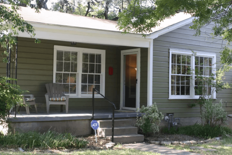 A small olive-green house with a front porch and two chairs in McLennan County, Texas.
