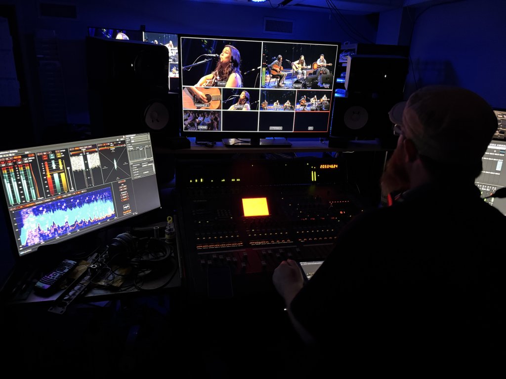 A person operating a professional audio mixing console in a dark studio control room in McLennan County, Texas.
