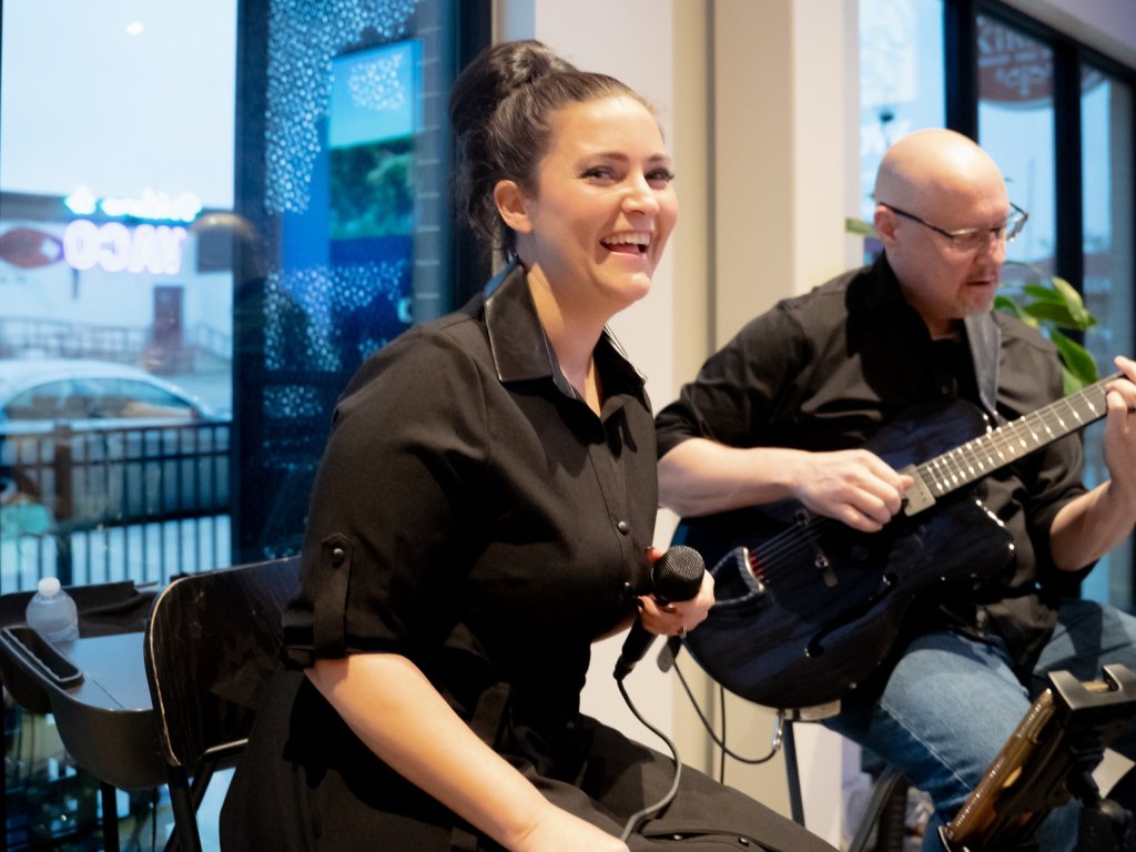 A woman singing into a microphone while a man plays an electric guitar in McLennan County, Texas.
