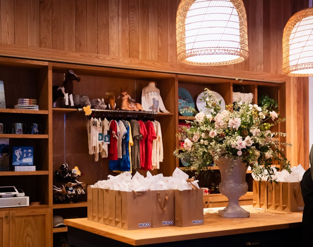 A retail shop counter with gift bags, a large floral arrangement, and wooden shelves in McLennan County, Texas.