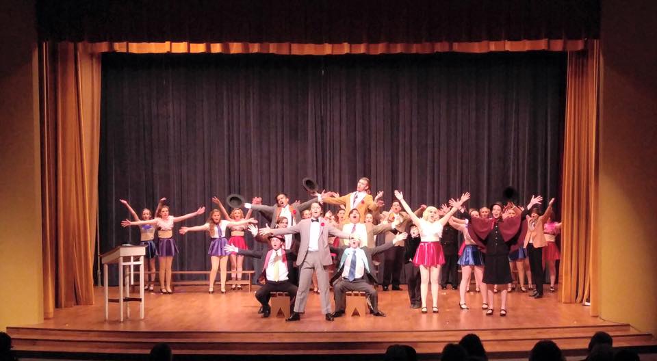 A large cast of performers in costumes singing and dancing on a theater stage in McLennan County, Texas.