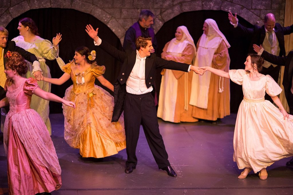 A man in a tuxedo dances with women in period dresses on a stage in McLennan County, Texas.