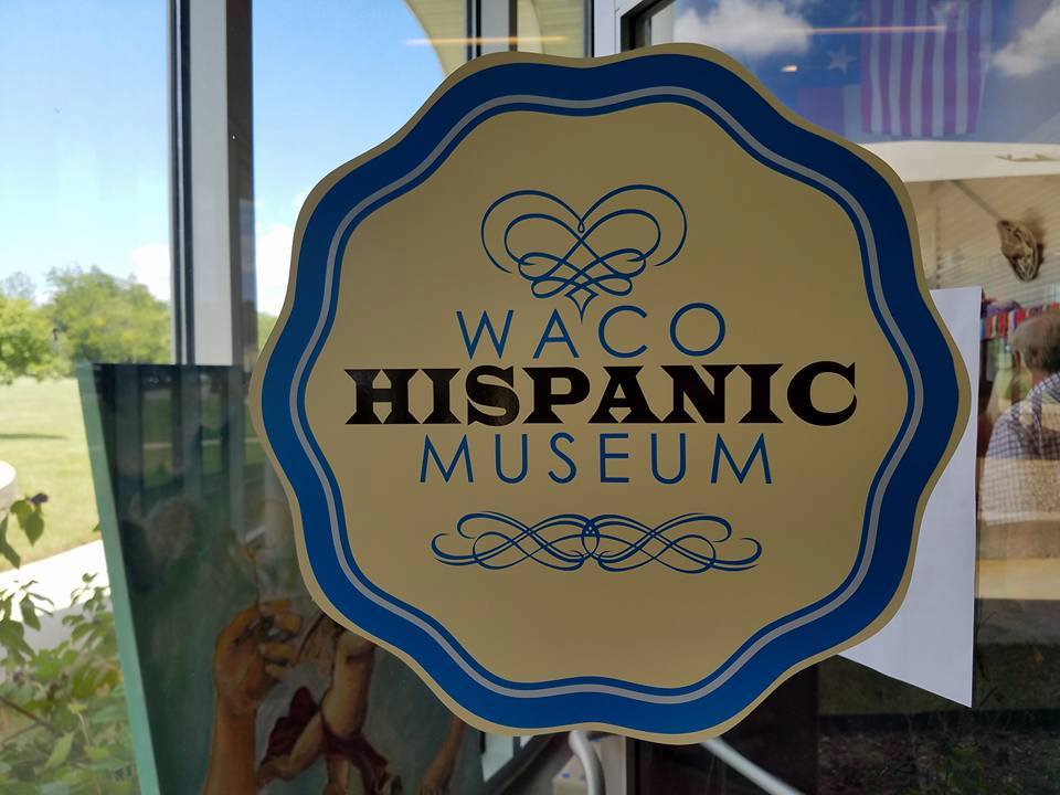 A decorative sign on a glass door for the Waco Hispanic Museum in McLennan County, Texas.