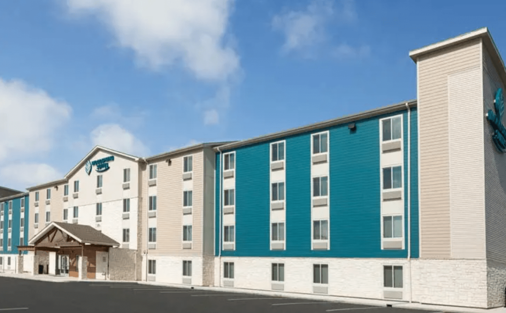 A modern WoodSpring Suites hotel building with blue and beige siding under a blue sky in McLennan County, Texas.