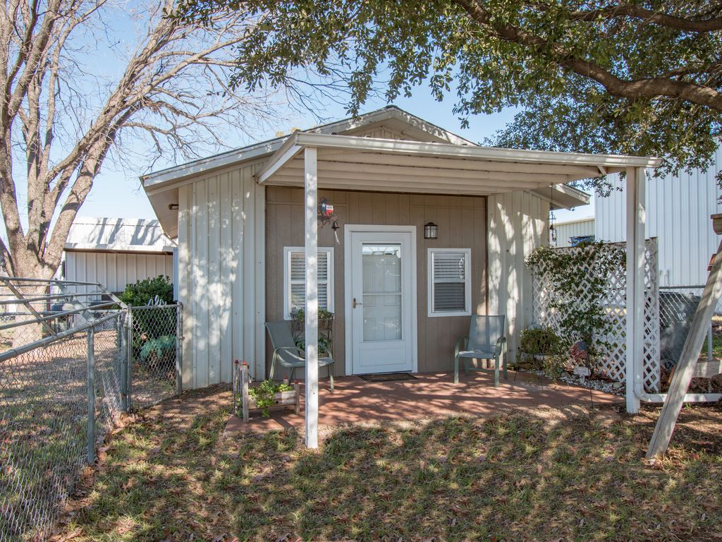 A small, tan-colored cottage with a covered front porch and two chairs in McLennan County, Texas.