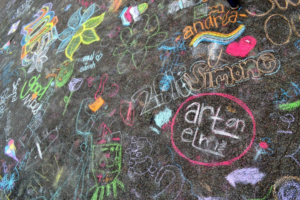 Colorful chalk drawings and messages written on a dark asphalt surface in McLennan County, Texas.