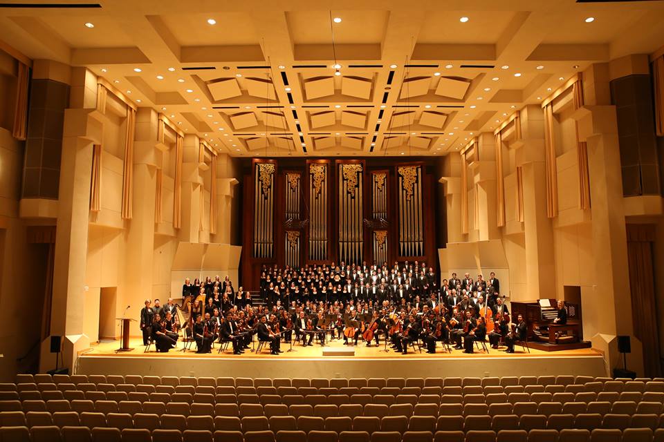 A large orchestra and choir performing on a stage in a concert hall in McLennan County, Texas.