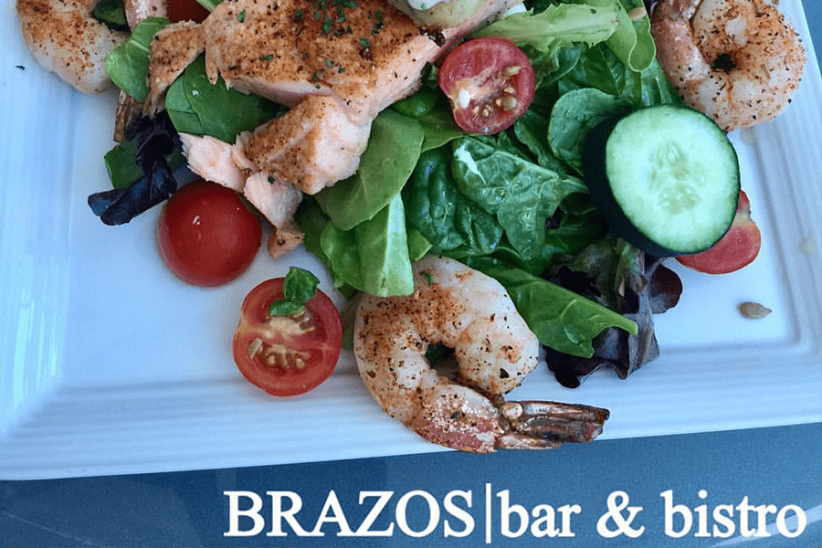 A fresh salad topped with grilled salmon and seasoned shrimp on a white plate in McLennan County, Texas.