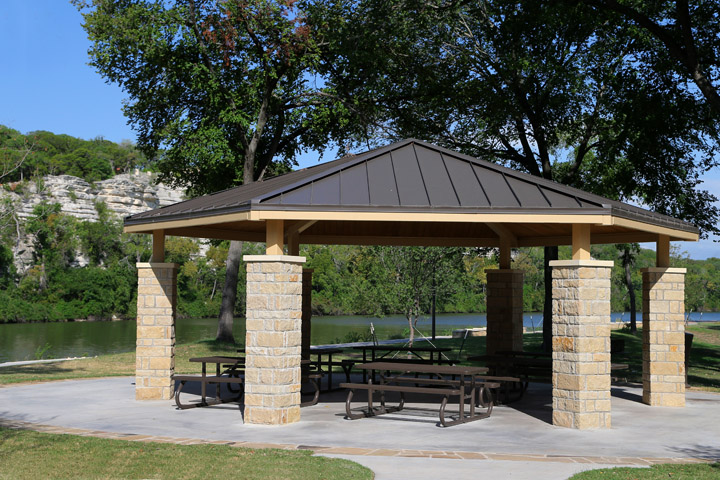A stone and metal pavilion with picnic tables overlooking a river and limestone cliffs in McLennan County, Texas.