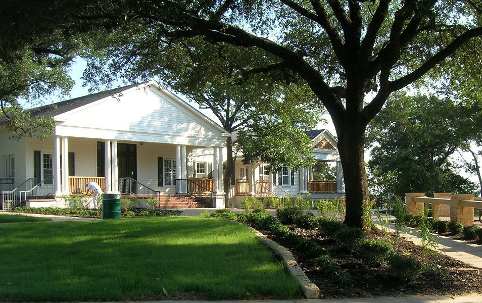 A white house with a porch and columns surrounded by large trees and grass in McLennan County, Texas.