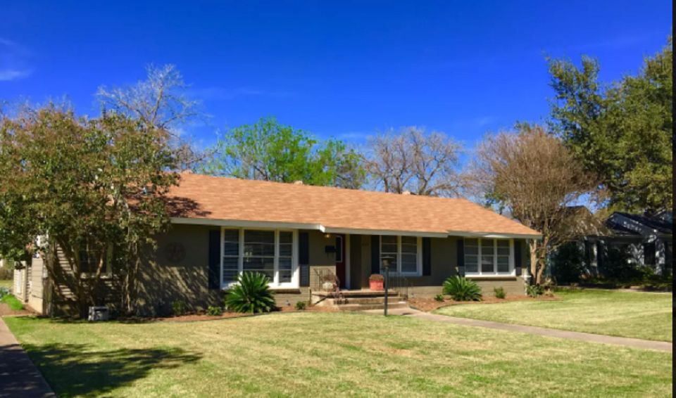 A single-story suburban house with a brown roof and green lawn under a blue sky in McLennan County, Texas.
