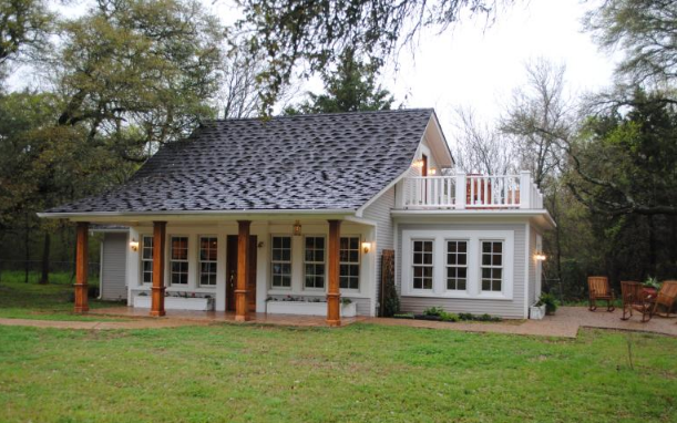 A charming cottage with a porch and a small balcony surrounded by trees in McLennan County, Texas.