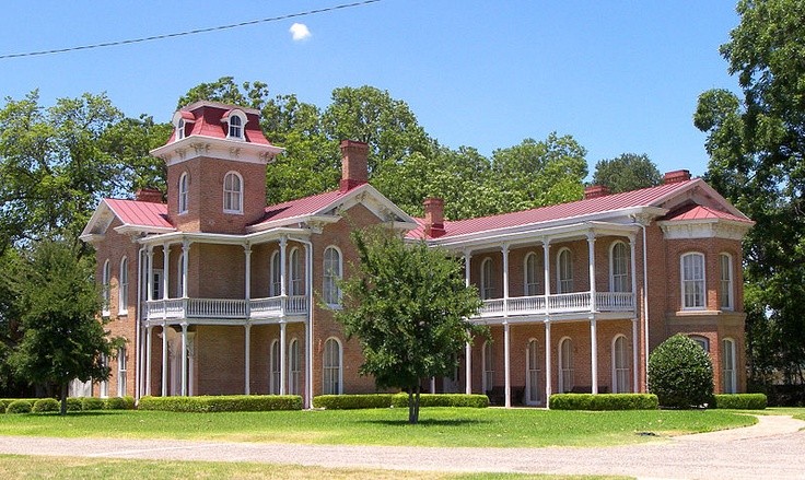 A historic two-story brick mansion with a red roof and wrap-around porches in McLennan County, Texas.