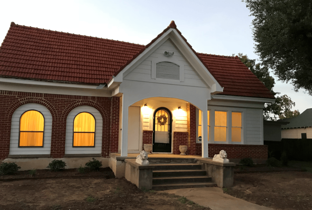 A brick house with a red tile roof and glowing windows at dusk in McLennan County, Texas.