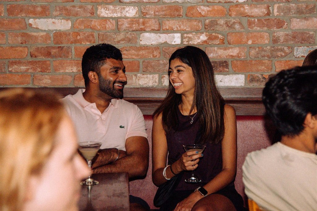 A man and woman smiling and talking while holding cocktails at a bar in McLennan County, Texas.