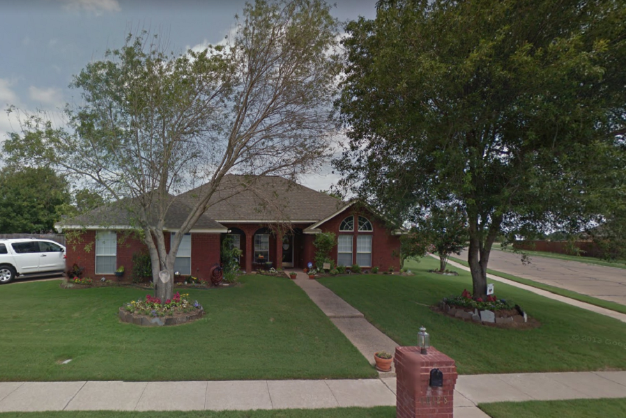 A single-story red brick house with a green lawn and two large trees in McLennan County, Texas.