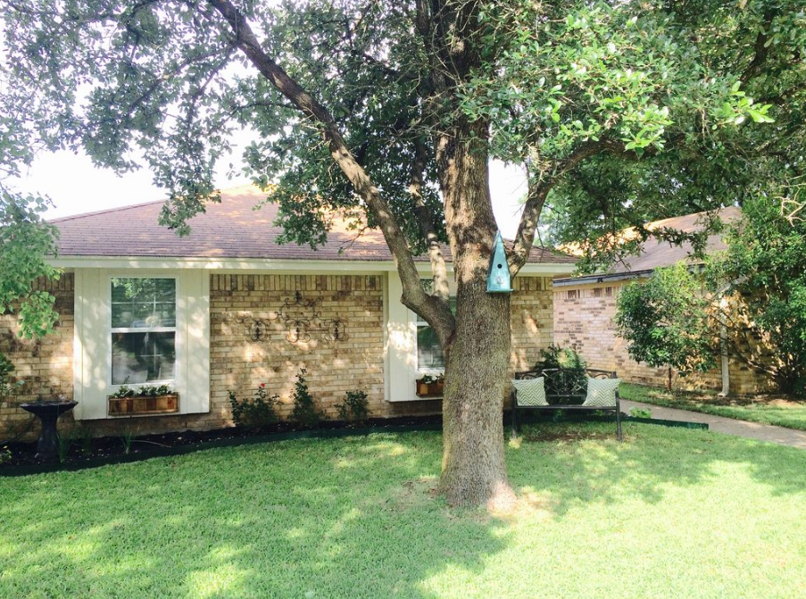 A brick house with a large tree in the front yard and a birdhouse in McLennan County, Texas.