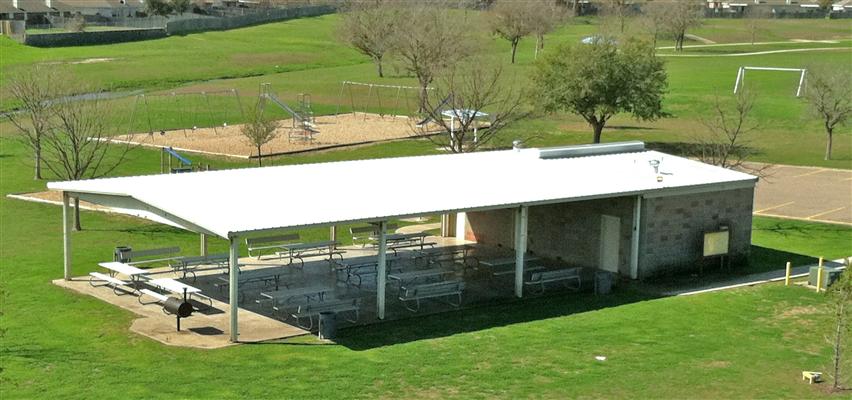An aerial view of a park pavilion with picnic tables and a nearby playground in McLennan County, Texas.