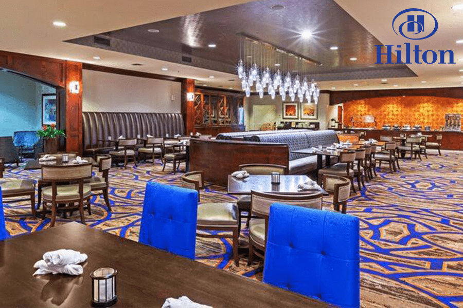 A spacious, modern hotel restaurant dining area with blue chairs and patterned carpet in McLennan County, Texas.