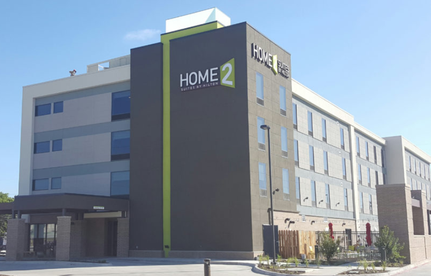 A modern Home2 Suites by Hilton hotel building under a clear blue sky in McLennan County, Texas.