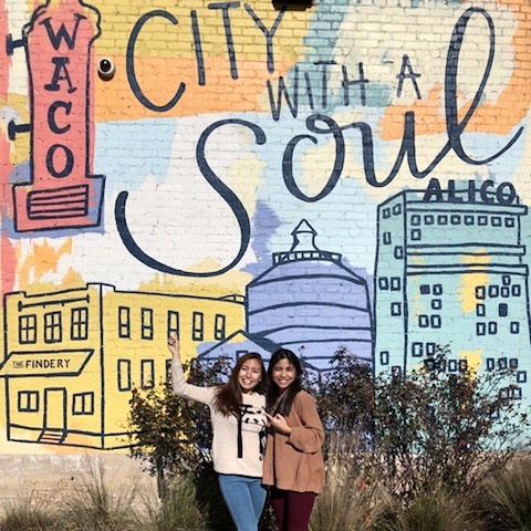 Two women posing in front of a colorful Waco city mural in McLennan County, Texas.