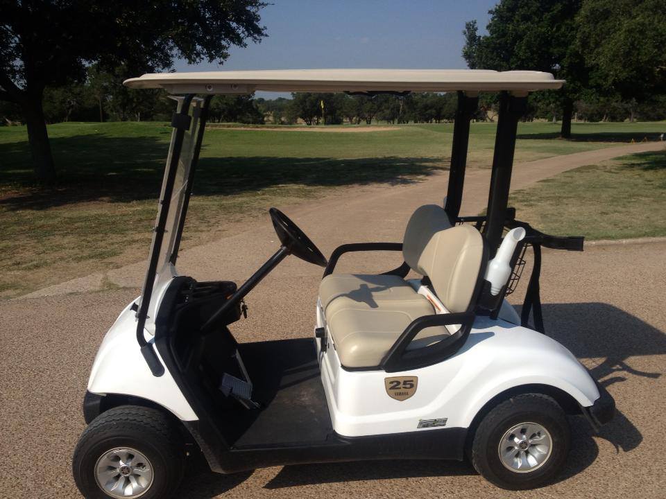 A white Yamaha golf cart parked on a paved path at a golf course in McLennan County, Texas.