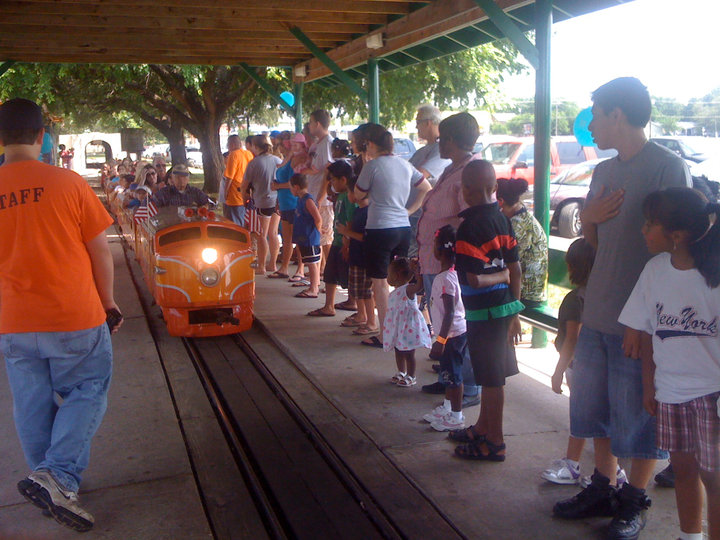 A group of people waiting for a small orange train at a station in McLennan County, Texas.