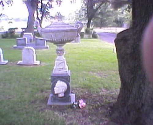 A stone urn monument with a carved portrait in a cemetery in McLennan County, Texas.