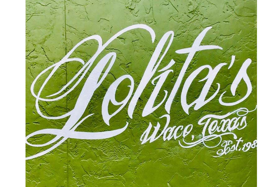 White cursive lettering on a textured green wall reading Lolita's Waco, Texas Est. 198 in McLennan County, Texas.