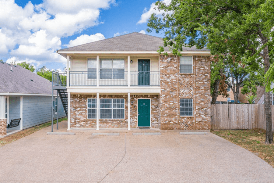 A two-story brick apartment building with a balcony and a concrete parking area in McLennan County, Texas.