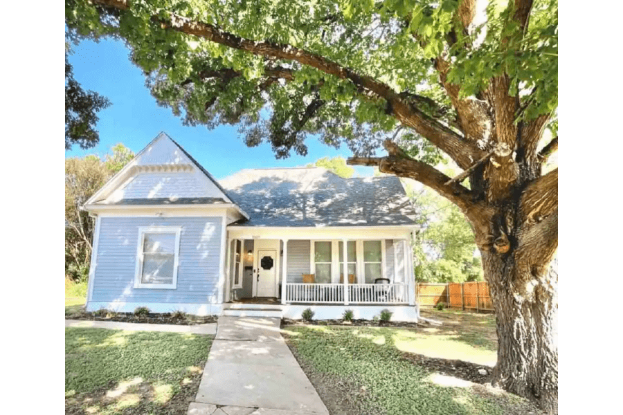 A charming light blue house with a front porch and a large tree in McLennan County, Texas.