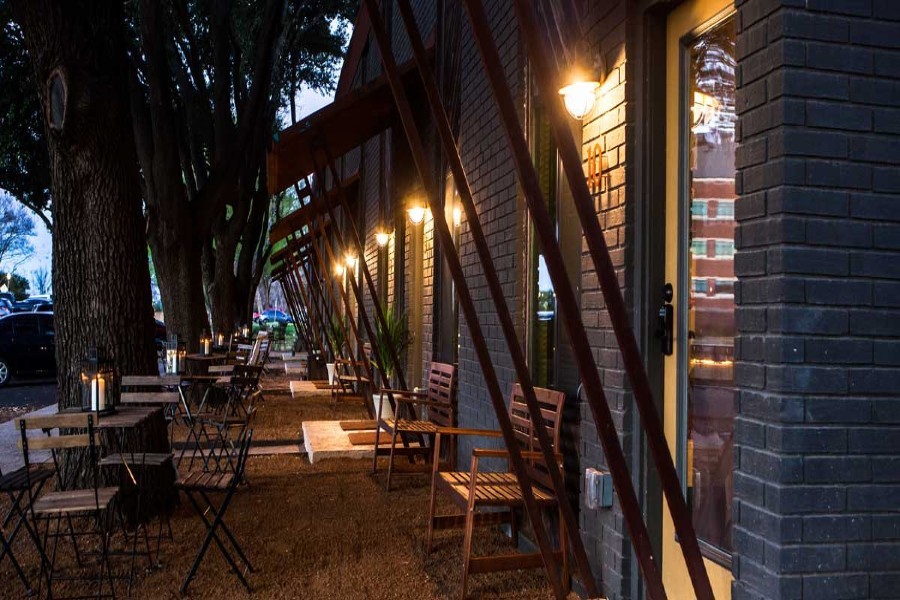 Outdoor patio seating area with wooden chairs and tables along a brick building at dusk in McLennan County, Texas.