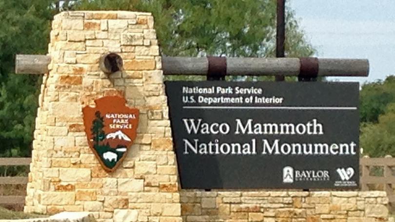 The entrance sign for the Waco Mammoth National Monument with a stone pillar in McLennan County, Texas.