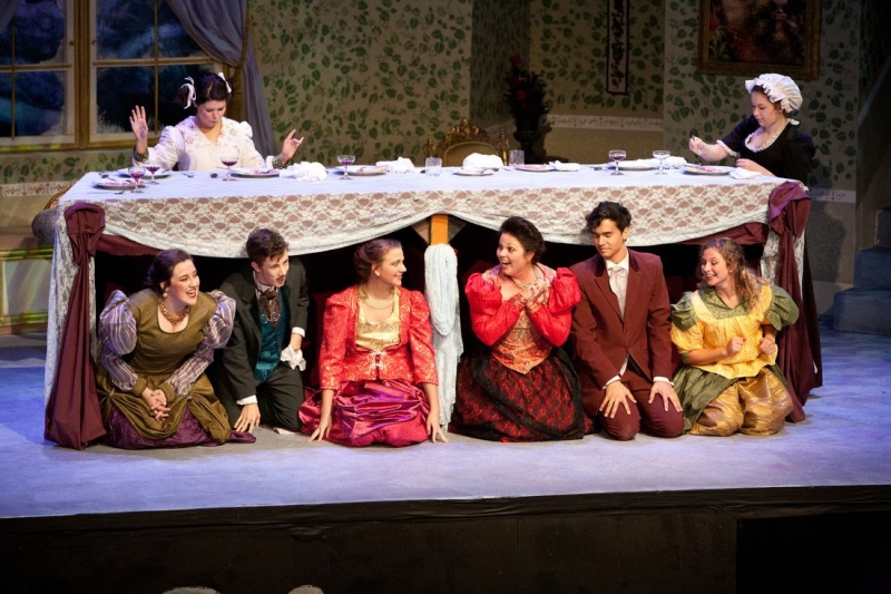 A group of actors in period costumes kneeling beneath a long dining table on stage in McLennan County, Texas.