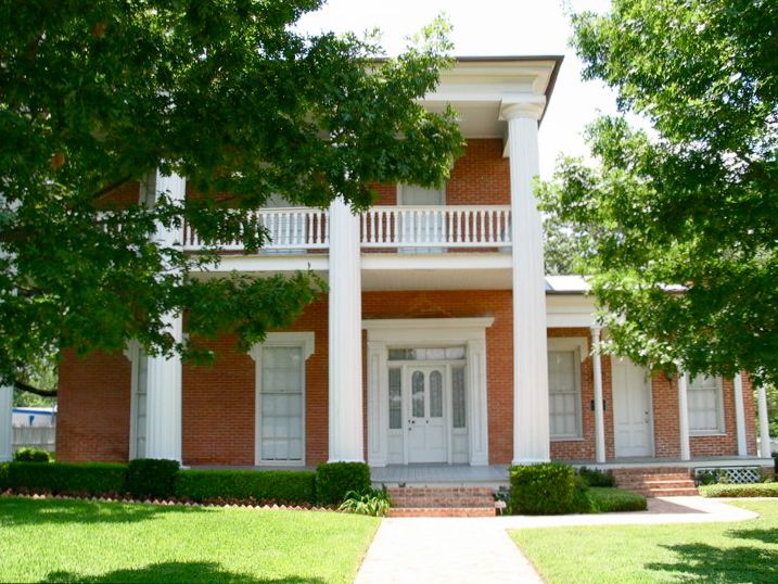 A historic two-story red brick house with white columns and a balcony in McLennan County, Texas.