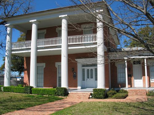 A historic two-story red brick house with white columns and a balcony in McLennan County, Texas.