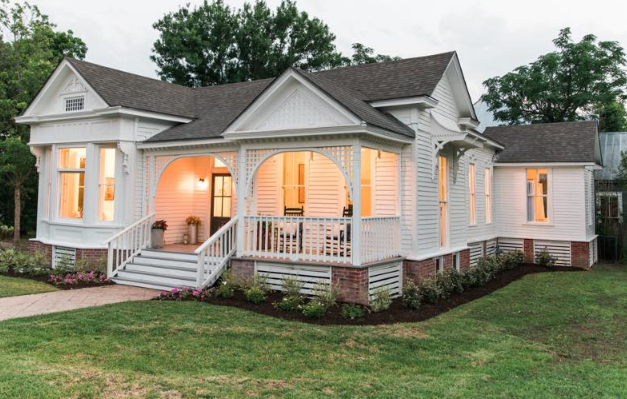 A charming white Victorian-style house with a welcoming front porch and warm interior lighting in McLennan County, Texas.