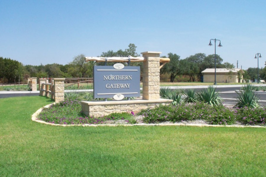 A stone sign reading Northern Gateway stands in a landscaped park area in McLennan County, Texas.