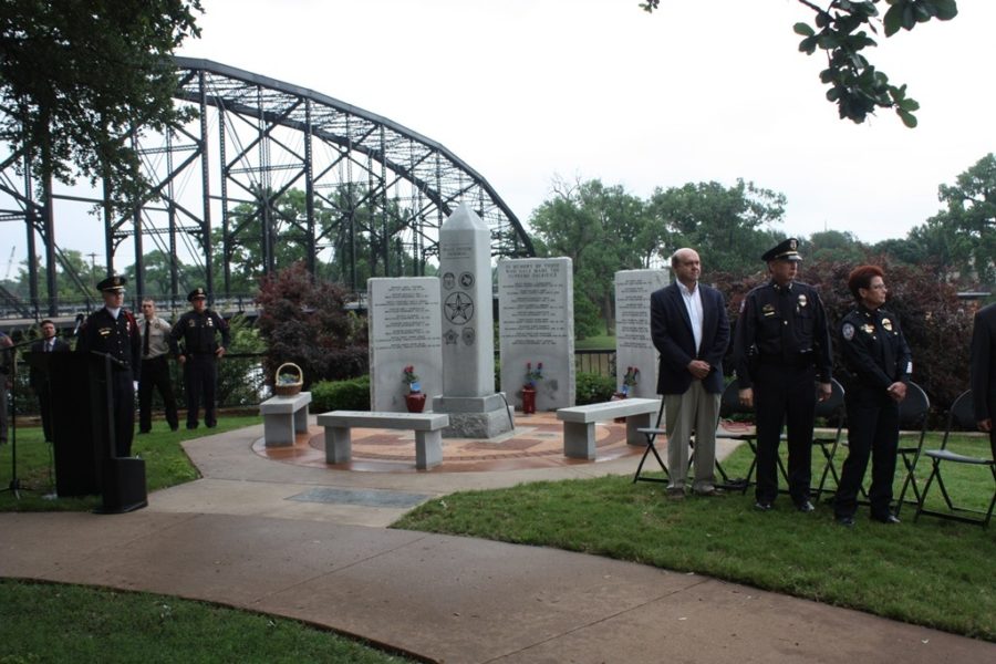Police officers and civilians gather at a memorial monument near a large steel bridge in McLennan County, Texas.