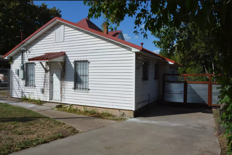 A small white house with a red roof and a metal gate in McLennan County, Texas.