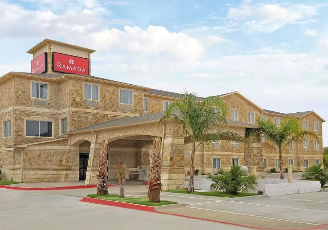 A stone-clad Ramada hotel building with a covered entrance and palm trees in McLennan County, Texas.
